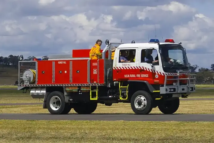 A white and red New South Wales Rural Fire Service heavy 4WD bushfire tanker parked on tarmac during emergency preparedness operations.