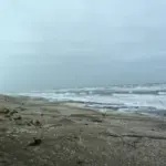 Churning grey seas and surf along a coastal beach during a storm.