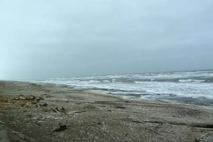Churning grey seas and surf along a coastal beach during a storm.