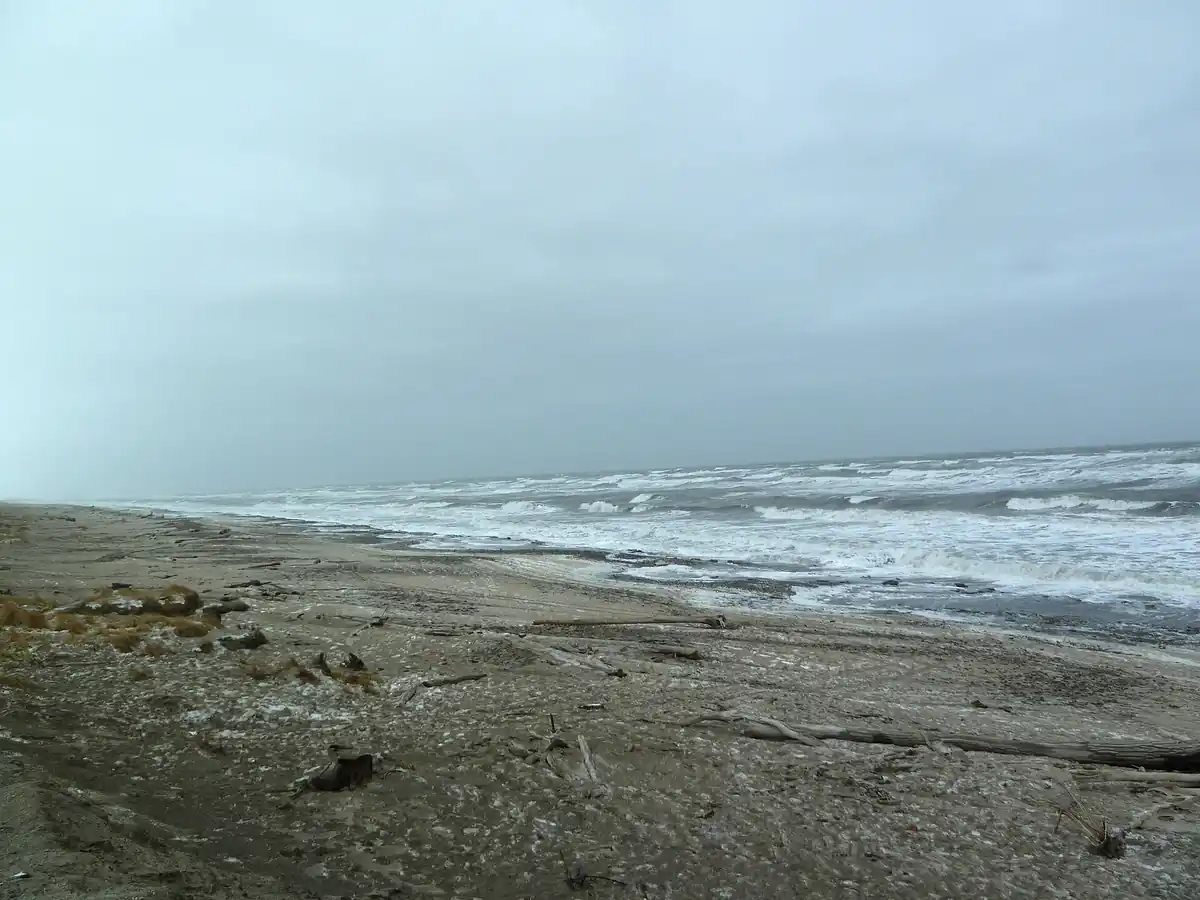 Churning grey seas and surf along a coastal beach during a storm.