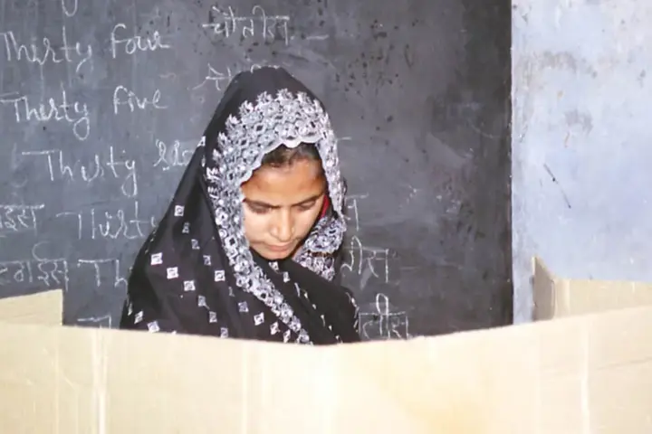 A woman in traditional attire casting her vote at a polling booth with election officials present