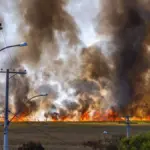 Wildfire burning across a rural field under a clear sky