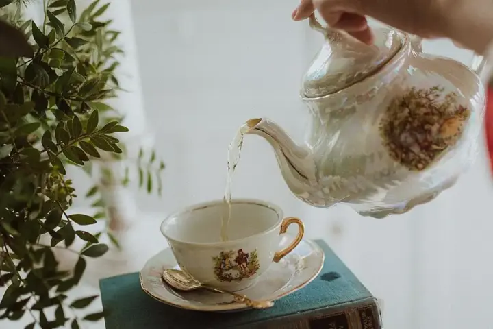 Tea being poured from a porcelain teapot into a small cup and saucer
