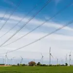 Wind turbines across a green field beside an electricity pylon and transmission lines