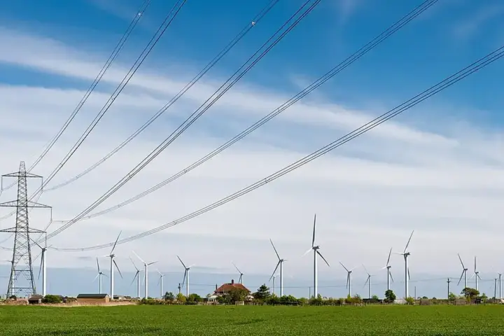 Wind turbines across a green field beside an electricity pylon and transmission lines