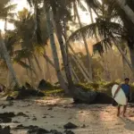 A surfer carrying a board walks along a palm-lined beach on Siargao Island in the Philippines