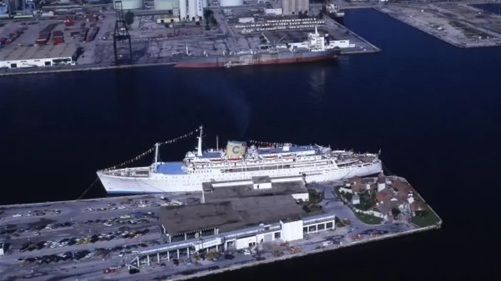 A large cruise ship moored at a port with passengers and a gangway