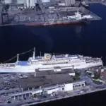 A large cruise ship moored at a port with passengers and a gangway