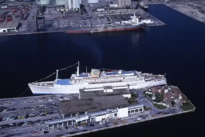A large cruise ship moored at a port with passengers and a gangway