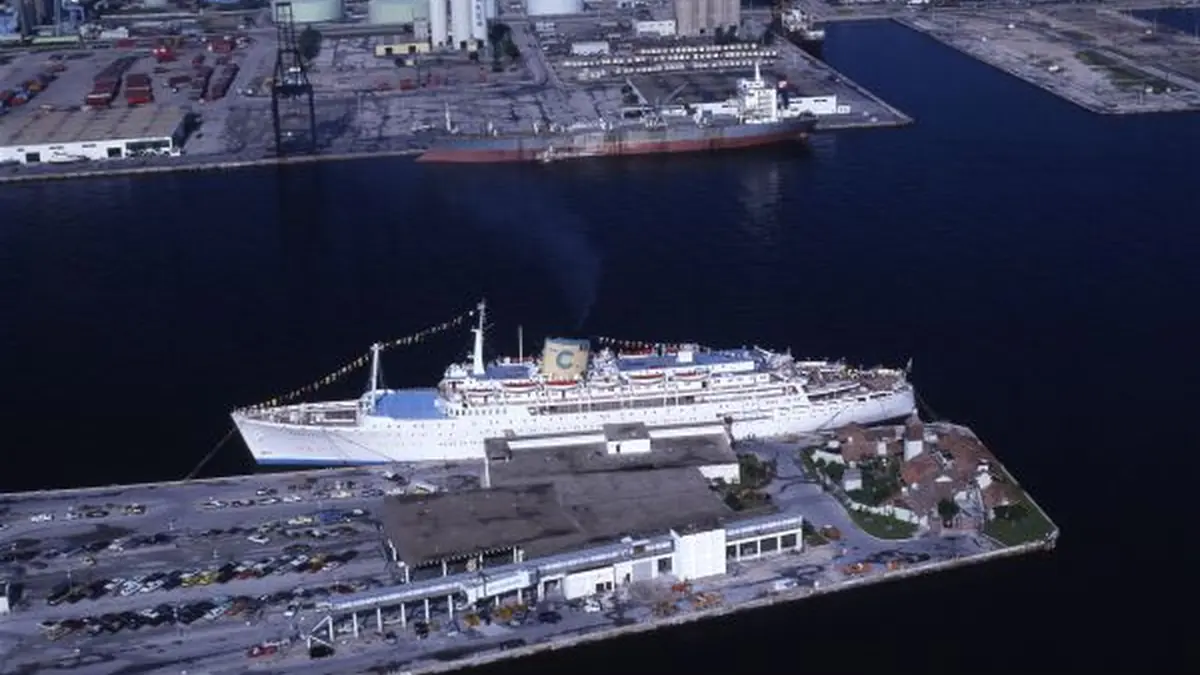 A large cruise ship moored at a port with passengers and a gangway