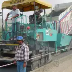 An asphalt paving machine spreading hot mix asphalt on a road construction site with crumb rubber blend visible