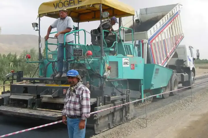 An asphalt paving machine spreading hot mix asphalt on a road construction site with crumb rubber blend visible