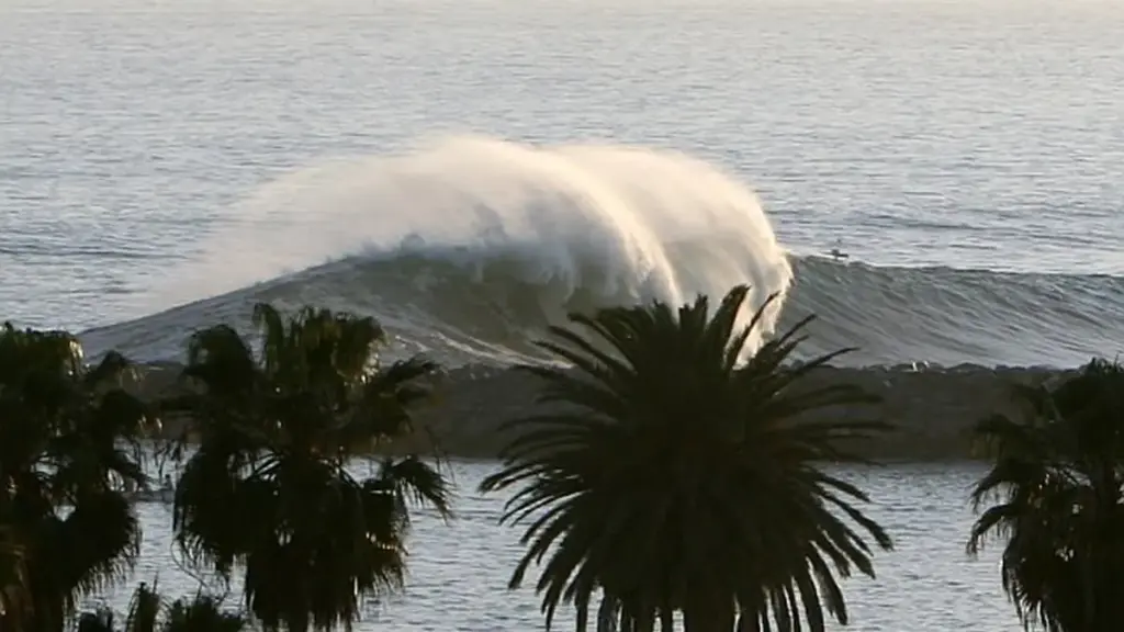 Powerful ocean wave cresting and breaking heavily against the sandy shoreline near coastal structures in Newport Beach, California.