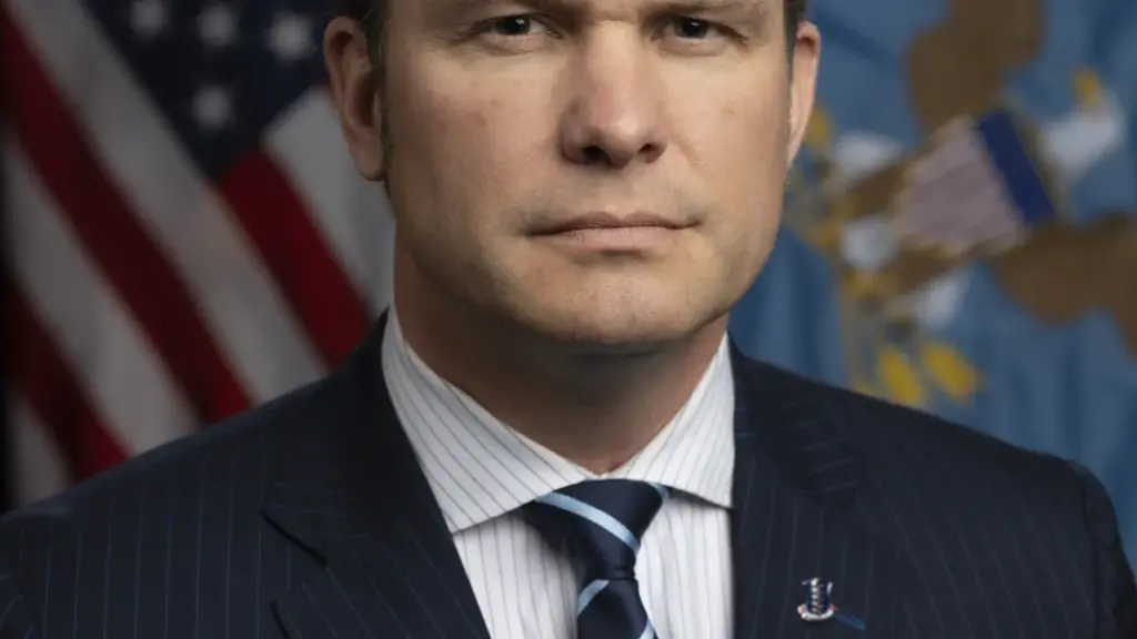 Formal photographic portrait of US Secretary of Defense Pete Hegseth standing before the United States and Department of Defense flags.