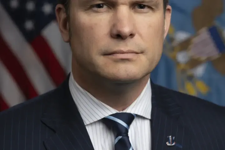 Formal photographic portrait of US Secretary of Defense Pete Hegseth standing before the United States and Department of Defense flags.