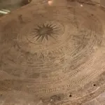 Detailed view of an ancient Vietnamese bronze drum displaying geometric patterns and central sunburst motifs.