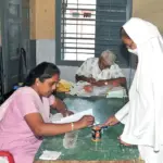 Close-up of an election official applying purple indelible ink to the index finger of a female voter at a ballot booth.