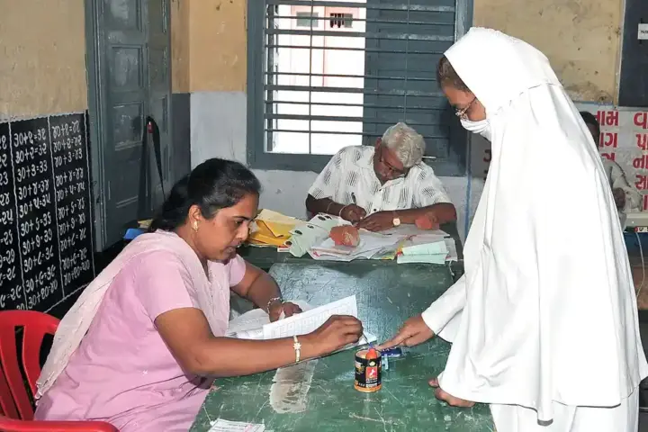 Close-up of an election official applying purple indelible ink to the index finger of a female voter at a ballot booth.