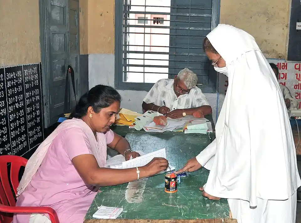Close-up of an election official applying purple indelible ink to the index finger of a female voter at a ballot booth.