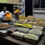 Traditional Indian sweet shop interior with containers of ghee and sweets arranged behind glass display counter