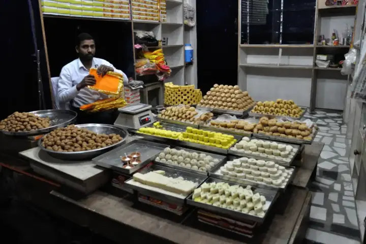 Traditional Indian sweet shop interior with containers of ghee and sweets arranged behind glass display counter