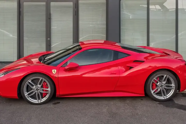 Red Ferrari 488 GTB sports car parked on asphalt, showing glossy paint, alloy wheels, and natural daylight reflections.