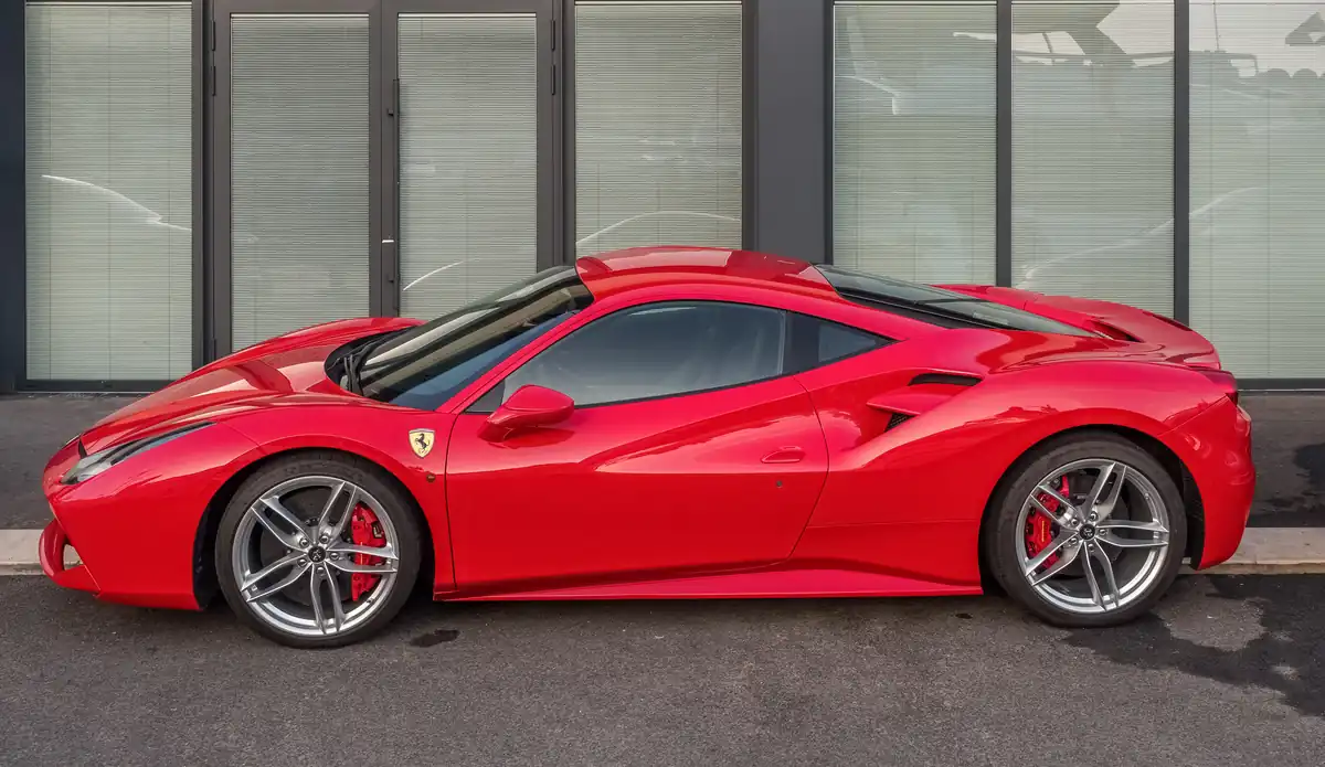 Red Ferrari 488 GTB sports car parked on asphalt, showing glossy paint, alloy wheels, and natural daylight reflections.