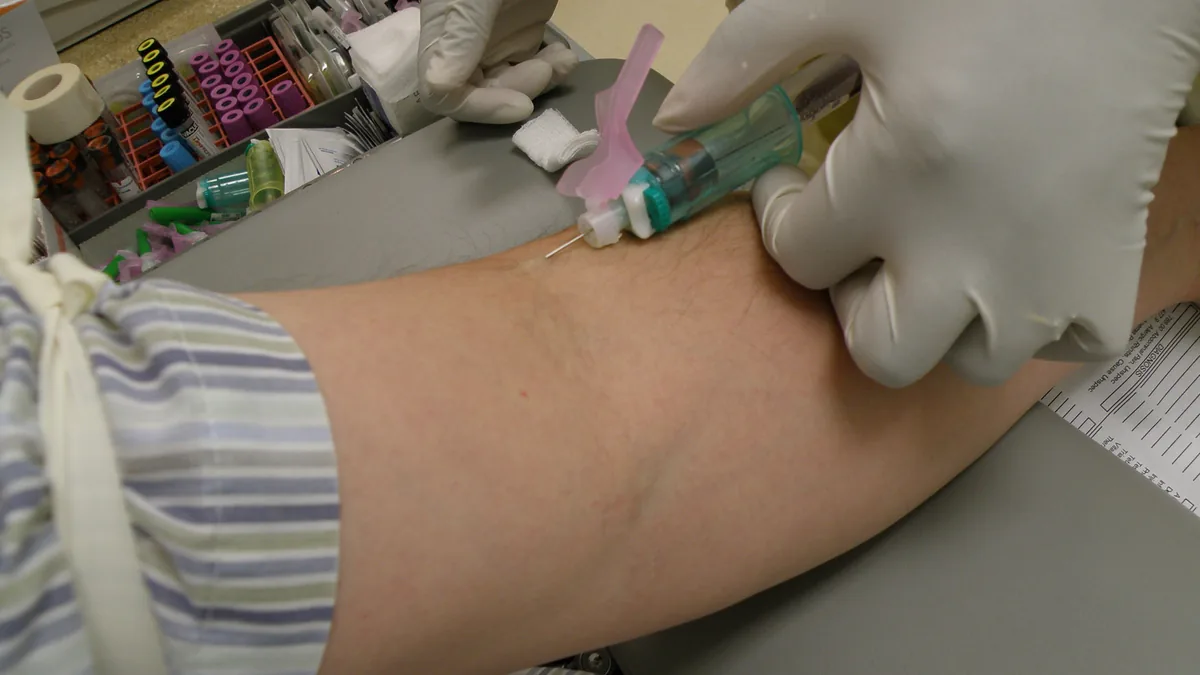 Photograph of a medical practitioner in sterile gloves drawing a venous blood sample into a vacutainer collection vial