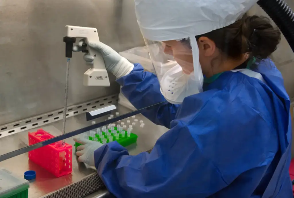 Researcher handling clinical vials and a precision pipette during peptide testing.