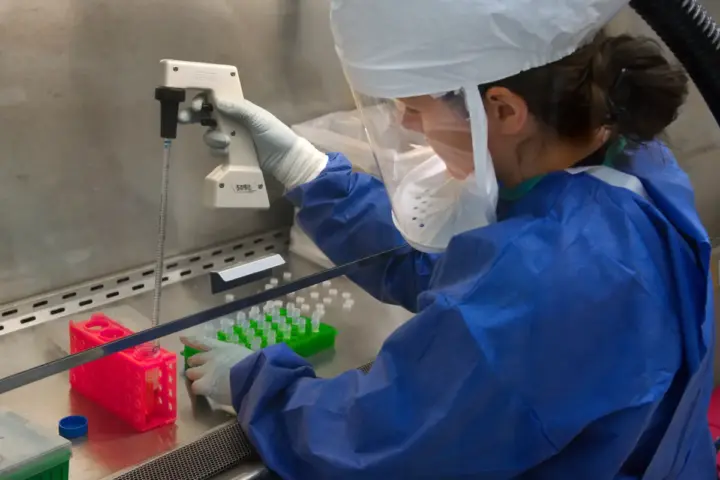 Researcher handling clinical vials and a precision pipette during peptide testing.