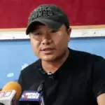 Man speaking at press conference with Impact News microphone flags