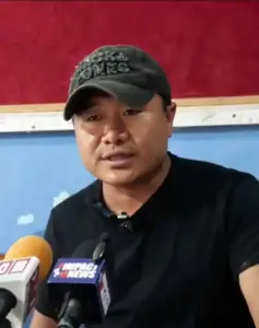 Man speaking at press conference with Impact News microphone flags