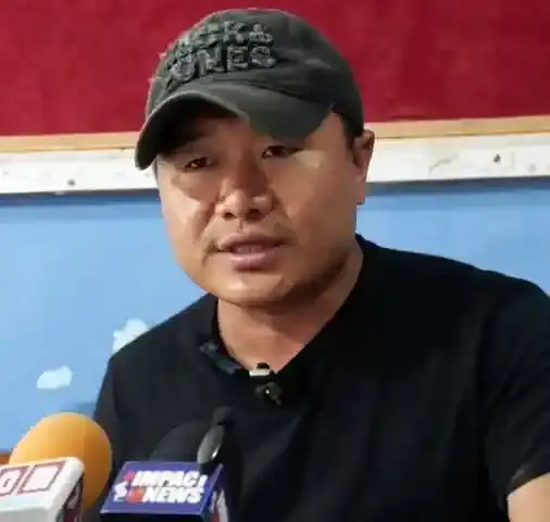 Man speaking at press conference with Impact News microphone flags