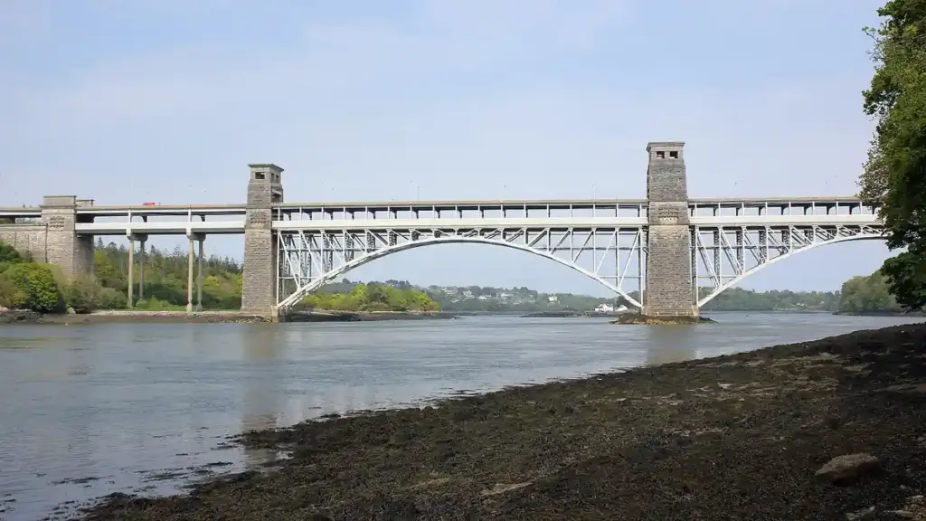 Britannia Bridge and Menai Strait under a cloudy sky, with green hills in the background, North Wales.