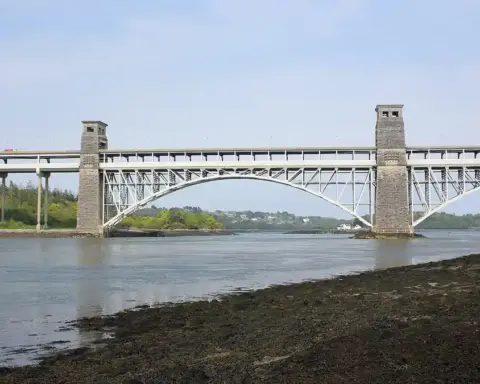 Britannia Bridge and Menai Strait under a cloudy sky, with green hills in the background, North Wales.