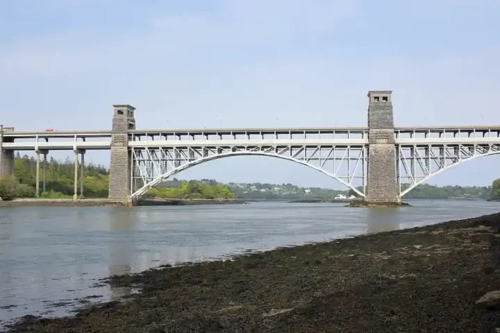 Britannia Bridge and Menai Strait under a cloudy sky, with green hills in the background, North Wales.