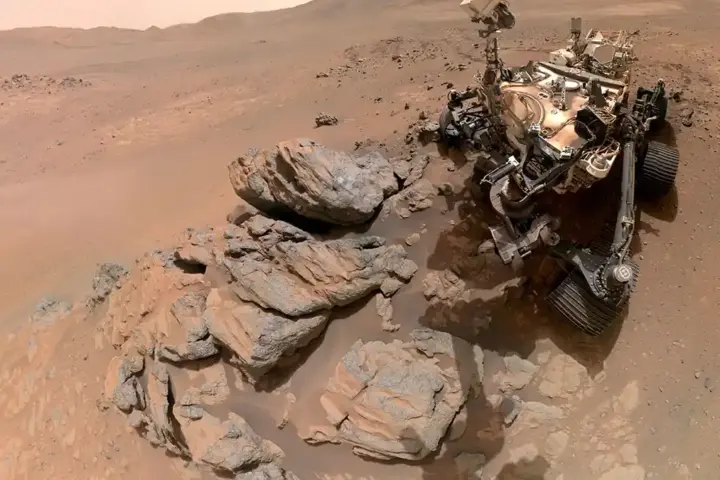 Photograph of NASA's Perseverance Mars rover beside rock outcrops on the surface of Jezero Crater during its dust analysis mission