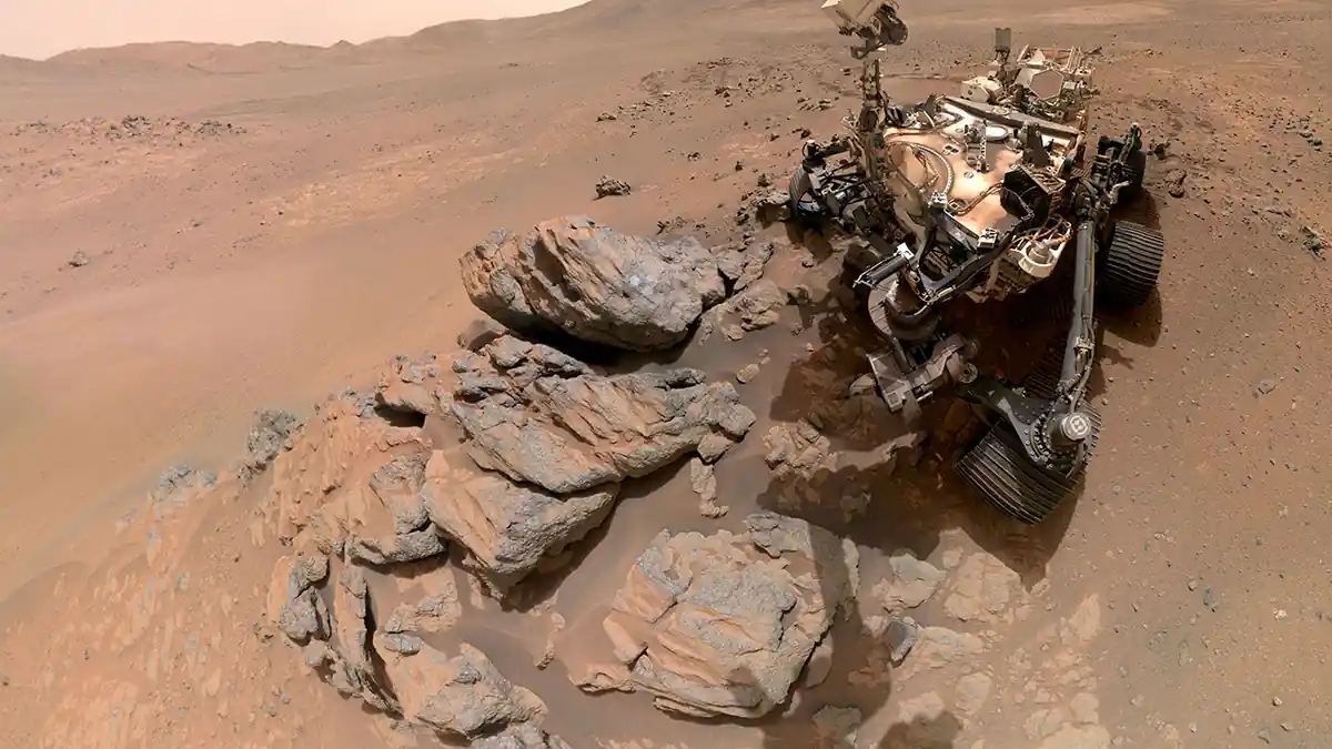 Photograph of NASA's Perseverance Mars rover beside rock outcrops on the surface of Jezero Crater during its dust analysis mission