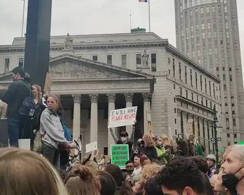 Large crowd of demonstrators gathered in lower Manhattan civic plaza holding signs and rallying for institutional accountability and survivor rights.