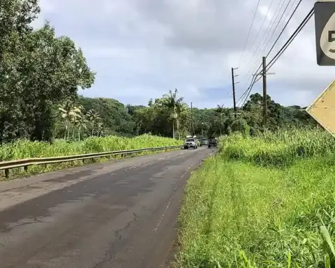 Hawaii State Route 560 running through the Hanalei Valley near the Hanalei River bridge, surrounded by steep green mountain peaks.