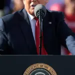 Former US President Donald Trump speaking into microphones at a podium during a political rally.
