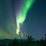 Bright green curtains of the aurora borealis glowing across a clear, dark night sky filled with stars.