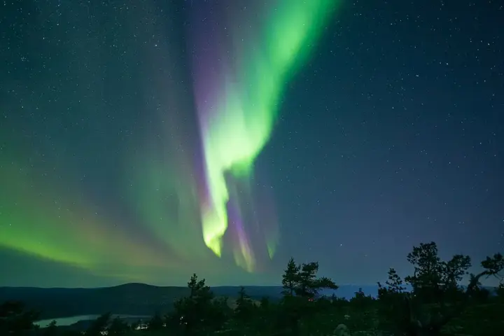 Bright green curtains of the aurora borealis glowing across a clear, dark night sky filled with stars.