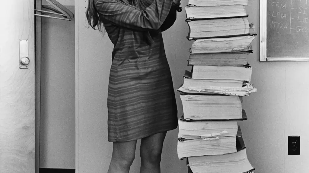 Margaret Hamilton standing in 1969 beside towering vertical stacks of Apollo 11 guidance software listings.