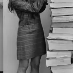 Margaret Hamilton standing in 1969 beside towering vertical stacks of Apollo 11 guidance software listings.