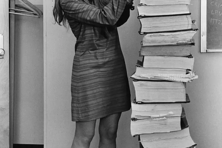 Margaret Hamilton standing in 1969 beside towering vertical stacks of Apollo 11 guidance software listings.