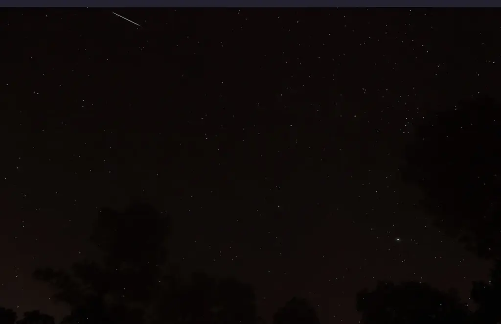 Night sky filled with stars and a sharp glowing trail of a meteor passing through the frame.