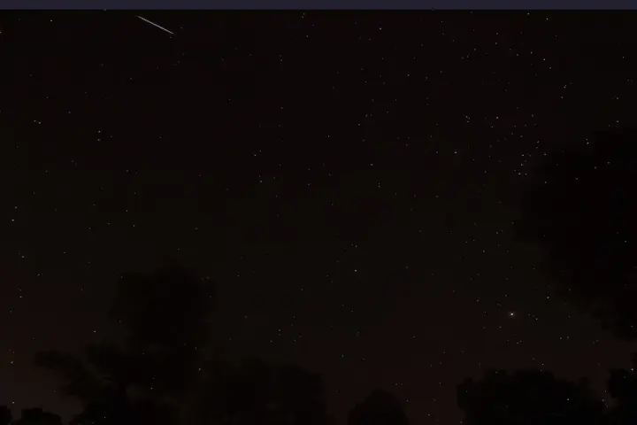 Night sky filled with stars and a sharp glowing trail of a meteor passing through the frame.