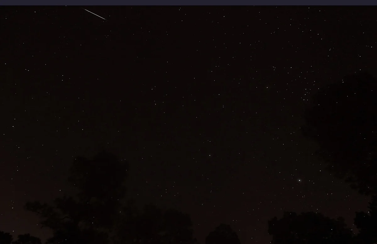 Night sky filled with stars and a sharp glowing trail of a meteor passing through the frame.