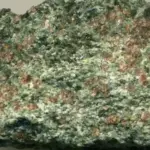 Close-up photograph of a red-and-green eclogite rock specimen with garnet crystals embedded in metamorphic minerals
